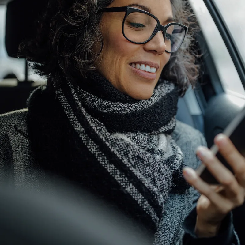 Library photo: a woman in a car smiling at her phone