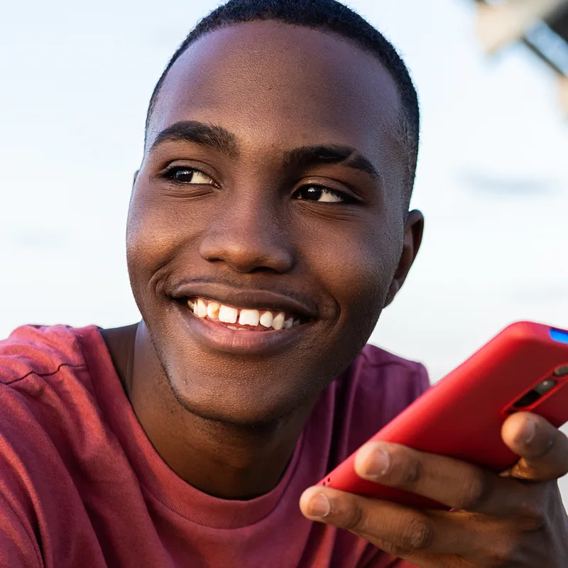 Library photo: a smiling young man holding a phone and a basketball